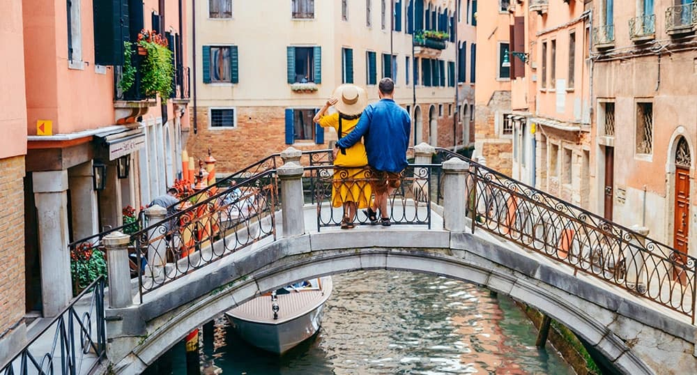 Couple stands on an arched Italian bridge, arms around each other