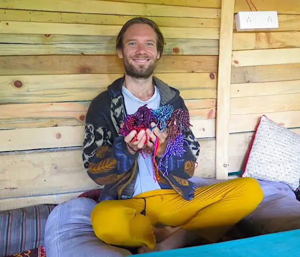 Man sits cross-legged on a couch holding hundreds of friendship bracelets