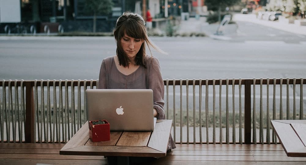 Woman sits at an outdoor cafe, typing on a laptop