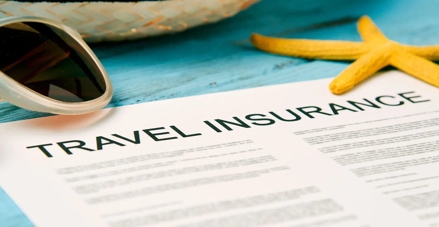 Travel insurance form laying on a blue table with sunglasses and starfish