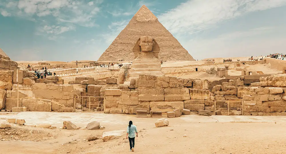 Man walks alone in the desert toward the Great Pyramid and Sphynx in Egypt