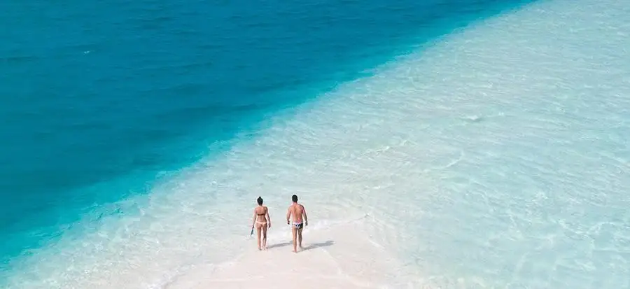 Couple walks on a beach with crystal-clear water