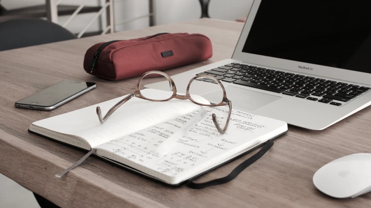 Notebook, laptop, and glasses sit on a desk