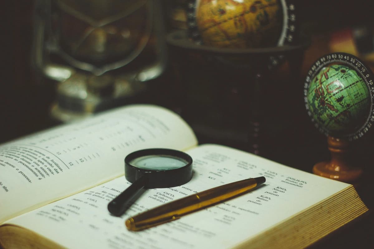 Book lays open with a pen and magnifying glass on top